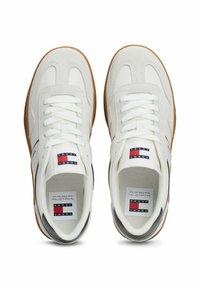 Sneaker bianche con tomaia in suede e pelle, suola in gomma, lacci piatti e branding che include elementi rossi e blu sulla linguetta.