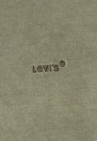 Tela verde oliva con una textura suave que presenta un logotipo de LeVi's® bordado en marrón. La superficie tiene un patrón de fina canalé.