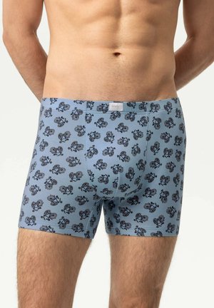 Man die lichtblauwe boxershorts draagt met een herhaald zwart fietsenpatroon, staand tegen een effen achtergrond.