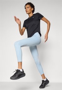 Fekete sportpóló, világoskék leggings hálós betétekkel és fekete sportcipők. Az öltözet sima, testhezálló kialakítással rendelkezik a mozgékonyság érdekében.