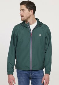 Grüne, leichte Jacke mit Kapuze, mit einem Reißverschluss vorne und kontrastierenden blauen und roten Streifen. Glatte Textur, lässige Passform.