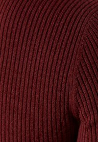 Suéter de punto burdeos con textura de canalé vertical, tejido suave, diseño ajustado y escote redondeado, que exhibe una apariencia cómoda y sin costuras.