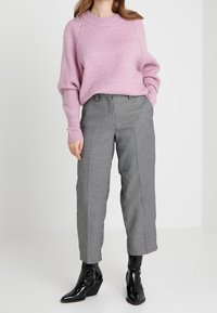 Suéter de canalé rosa claro de corte holgado y cuello redondo, combinado con pantalones con estampado de pata de gallo en blanco y negro y botas negras de tobillo.