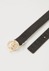 Zwarte faux leren riem met krokodillenstructuur, voorzien van een gouden ronde gesp met een in elkaar grijpend "MK"-logo en een verstelbare pin.