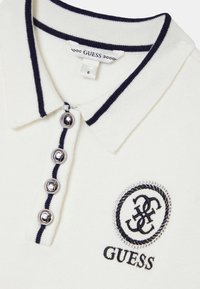 Polo blanc avec bordure marine, quatre boutons argentés et logo brodé. Conçu avec un col classique et une texture douce. Étiquette de taille visible.