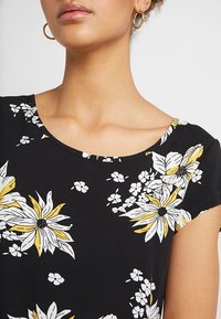 Sort blomsterbluse med store hvide og gule blomster, korte ærmer og rund halsudskæring. Glat stof med en subtil tekstur.