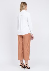 Camicia bianca a maniche lunghe con colletto, vestibilità comoda; abbinata a pantaloni a vita alta a sigaretta color ruggine e tacchi neri con cinturini.