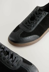 Svarta sneakers med en kombination av slät läder och mocka, med en texturerad yta, perforerade detaljer och gummisulor.