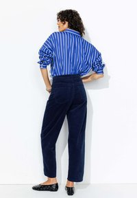Chemise oversized rayée bleu et blanc, assortie à un pantalon large en velours côtelé bleu marine. Ballerines noires avec des clous décoratifs. Tissus texturés.