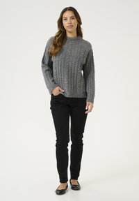 Pull en coton gris côtelé avec un col montant, orné de perles, associé à un pantalon noir slim et des chaussures plates noires.
