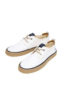 Scarpe di tela bianche con dettagli marroni, dotate di una suola in juta intrecciata, finiture blu navy e lacci beige, progettate per un uso quotidiano.