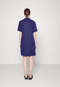 Vestido de manga curta e colarinho em azul marinho profundo, feito de um tecido suave, com um corte reto e comprimento até ao joelho. Sandálias de plataforma pretas incluídas.