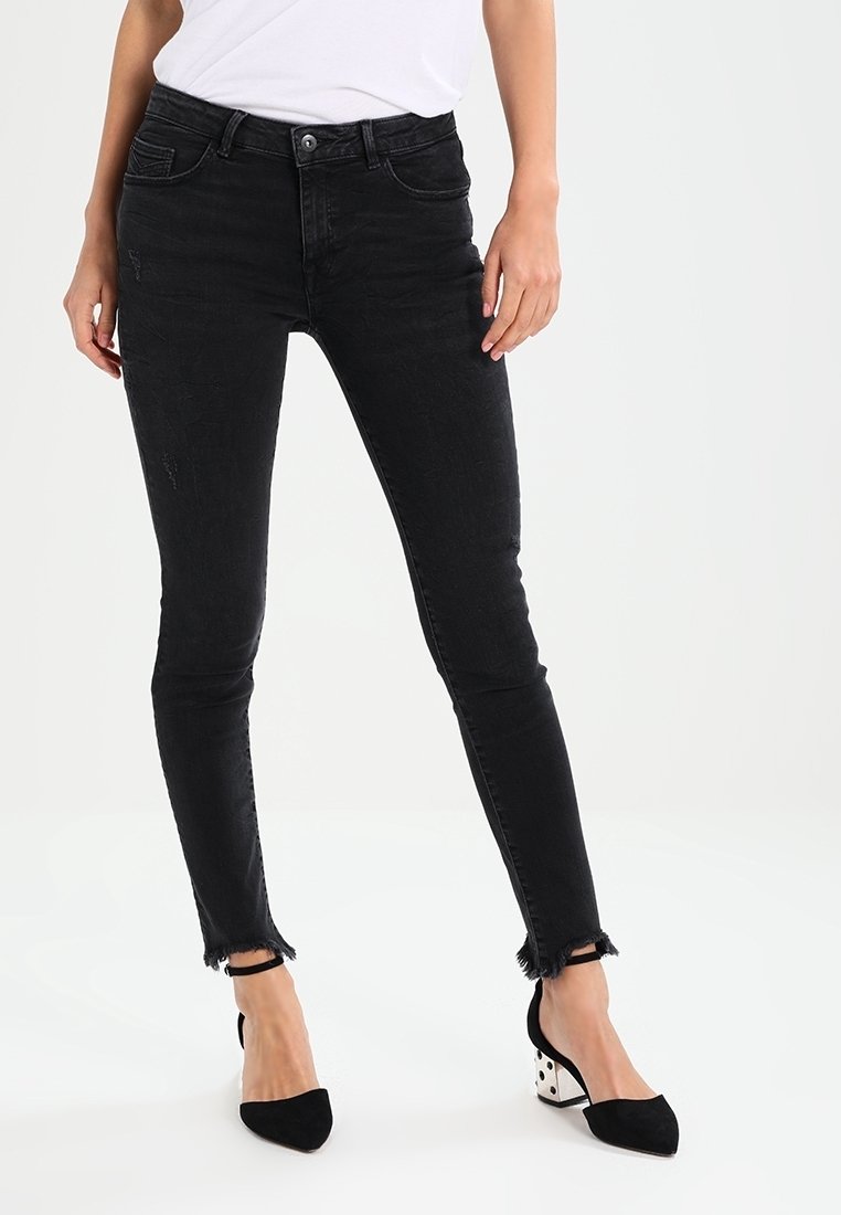 Czarne wąskie dżinsy z postrzępionym dołem i wyblakłą teksturą, połączone z czarnymi szpilkami z kontrastowym białym wzorem w kropki na obcasie.