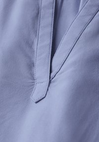 Tessuto azzurro chiaro caratterizzato da una texture liscia, con una piega delicata e un collare a punta vicino all'escollatura.