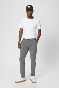 Grijze op maat gemaakte broek met een subtiele textuur, gecombineerd met een plain wit T-shirt en beige sneakers. De pet is zwart met een logo-detail.