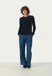Marineblauer, langärmeliger Strickpullover kombiniert mit lockeren, hochgeschnittenen blauen Jeans. Glatte Textur mit seitlichen Taschen, abgerundet mit schwarzen Schuhen.