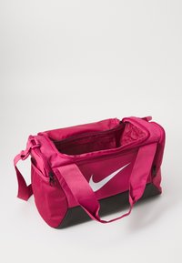 Ružový športový vak Nike s čiernym dnom, štvrcový tvar, veľká hlavná priehradka a biele logo na boku. Súčasťou sú nastaviteľné popruhy.