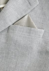 Blazer gris clair texturé avec un mouchoir de poche en soie gris clair assorti, plié dans la poche poitrine.