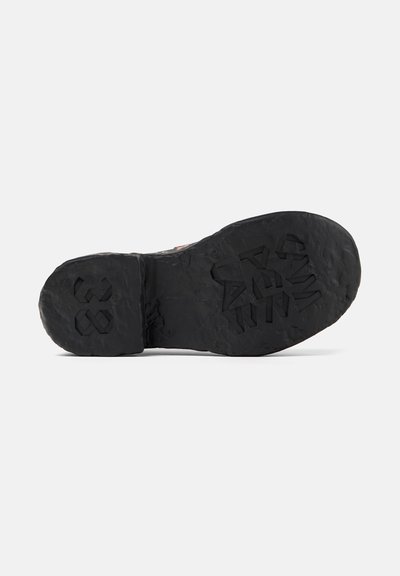 Black rubber shoe sole with textured patterns. Features embossed logos and uneven surface for traction. Overall sturdy design.