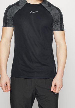 Personne athlétique portant un t-shirt noir Nike à manches courtes avec des épaules sombres à motifs et un short noir assorti.