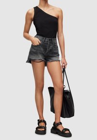 Top de canalé negro de un solo hombro, pantalones cortos de mezclilla gris cortados con dobladillo deshilachado, sandalias de plataforma negras, sosteniendo un bolso tote negro.