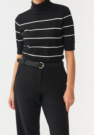 Sort turtleneck-trøje med hvide striber og korte ærmer. Kombineret med sort, højtaljede bukser og et sort bælte med gulddetaljer.