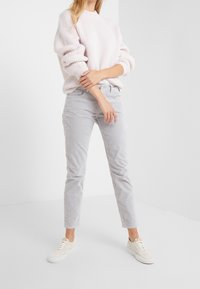 Jasnoróżowy sweter z prążkowanej dzianiny z opadającymi ramionami, w zestawieniu z jasnoszarymi, zwężanymi spodniami z miękkiego materiału oraz białymi trampkami.