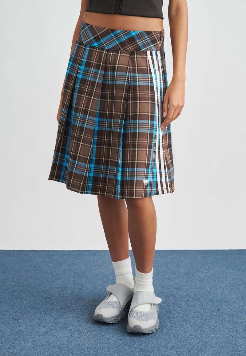 Καφέ καρό φούστα με μπλε λεπτομέρειες, πιετέ σχέδιο και λευκές πλαϊνές ρίγες. Συνδυασμένη με γκρι παπούτσια και λευκές κάλτσες.