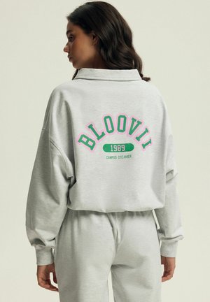 Szary sweter i pasujące spodnie z kolorową grafiką na plecach, która brzmi "BLOOVII 1989 CAMPUS DREAMER". Luźny krój i miękka struktura.