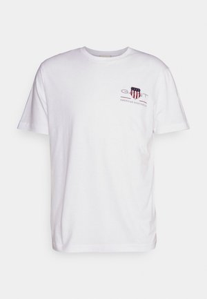 Bijela pamučna majica s okruglim izrezom, kratkim rukavima, i printanim logotipom s crvenim i plavim detaljima na lijevoj strani prsnog područja.