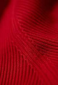 Primo piano di un tessuto a maglia rosso con texture, caratterizzato da costine verticali e intricati motivi tessuti che creano profondità e calore.