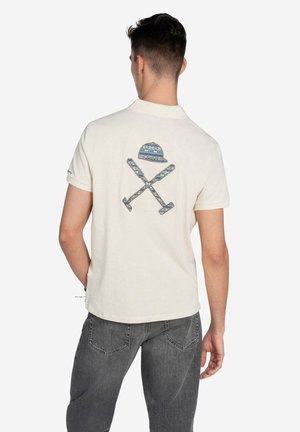 Camisa polo de manga corta color crema con un diseño bordado en la parte posterior que presenta un sombrero y remos cruzados en patrones azules.
