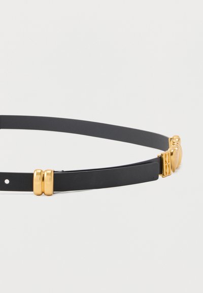 Μαύρη λεπτή ζώνη με γυαλιστερή χρυσή αγκράφα διπλού κρίκου και διακοσμητικές χρυσές λεπτομέρειες σε λείο δερμάτινο υλικό.