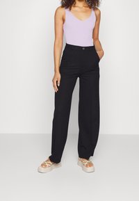 Czarne, szerokie spodnie o wysokim stanie, zestawione z fioletowym topem z prążkowanej dzianiny. Uzupełnione beżowymi sandałami na platformie z zielonymi paskami.