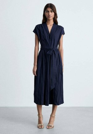 Robe midi bleu marine avec un design enveloppant, des manches courtes et une taille nouée, présentant une texture froissée et une silhouette fluide.