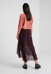 Gonna lunga e fluente di un viola scuro con motivo a pois, abbinata a una blusa leggera color corallo. Tessuto trasparente e testurizzato con orlo a strati.