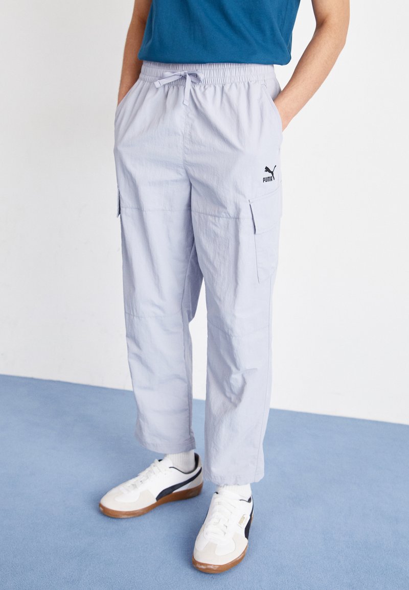 Lichtgrijze cargo broek met een elastische tailleband, zijzakken en een klein zwart logo. Gecombineerd met witte en marineblauwe sportschoenen.