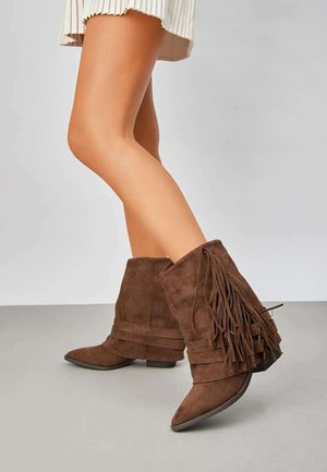 Bottines en suède marron avec un accent frangé, bout pointu et un petit talon. Présente des sangles superposées autour de la tige pour plus de détails.