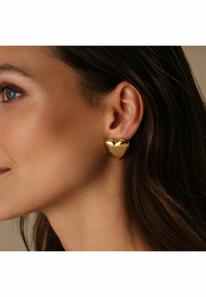 Guld øreringe i hjerteform med en blank overflade, der viser en glat tekstur og runde kanter, båret på venstre øre.