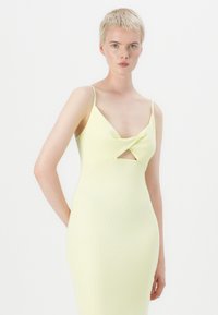 Robe jaune moulante avec un décolleté torsadé, des bretelles spaghetti et une longueur mi-mollet, fabriquée en tissu tricoté côtelé.