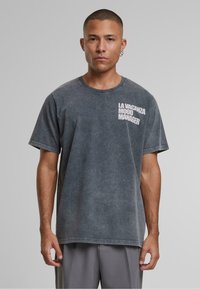 Grafitowy, krótki t-shirt wykonany z bawełny o luźnym kroju. Z przodu, na lewej piersi, umieszczony jest biały napis "LA VACANZA MOOD MANAGER".