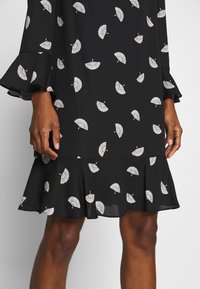 Svart klänning med vitt fläktmönster, tillverkad av ett lätt material. Har klockärmar och en utställd nederkant.