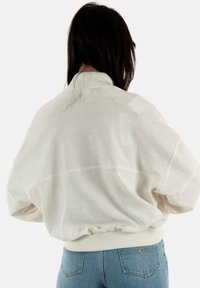Suéter de forro polar blanco con un cuello alto, hombros caídos, dobladillo elástico y puños de canalé. Llevado con jeans de mezclilla azul.