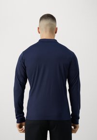 Marineblå langærmet polo-skjorte, glat stof, klassisk krave, tætsiddende design med lige kant, og minimal detaljer.