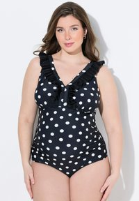 Maillot de bain noir à pois blancs, avec un décolleté en V profond, des bretelles froncées et des côtés froncés pour un design ajusté.