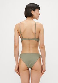 Olíva zöld bikini szett, egyszerű dizájnnal, vékony állítható pántokkal és minimális lefedettségű bugyival. Zökkenőmentes, rugalmas anyagtextúra.