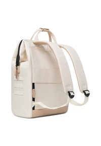 Mochila rectangular beige con cremallera negra, correas ajustables y panel texturizado. Cuenta con correas decorativas y acentos suaves.