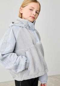 Ljusgrå huvtröja med en fluffig textur, med dragkedja, stor framficka och släta ärmar med logodetalj.