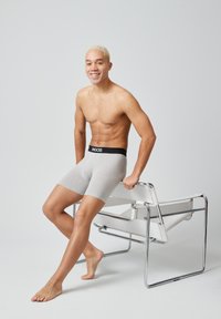 Boxer da uomo grigi con cintura nera etichettata "SNOCKS", indossati da una persona seduta su una sedia moderna in cromo, su sfondo semplice.