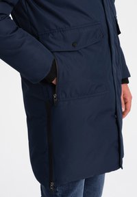 Námořnická bunda s texturovanou látkou, zipovými bočními kapsami a kapsou na klopě. Obsahuje zip a černé kovové doplňky.